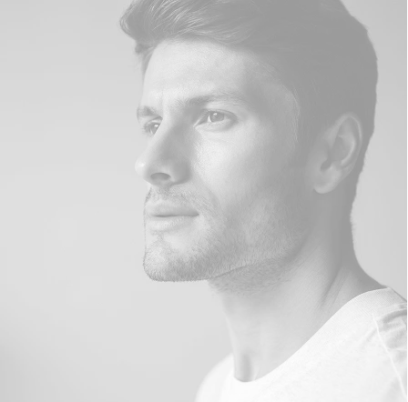 A black and white profile close-up of a handsome man with styled hair and light stubble, looking off into the distance.