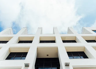 A low-angle shot of a bright white, modern building exterior with repeated vertical lines against a blue sky with white clouds.
