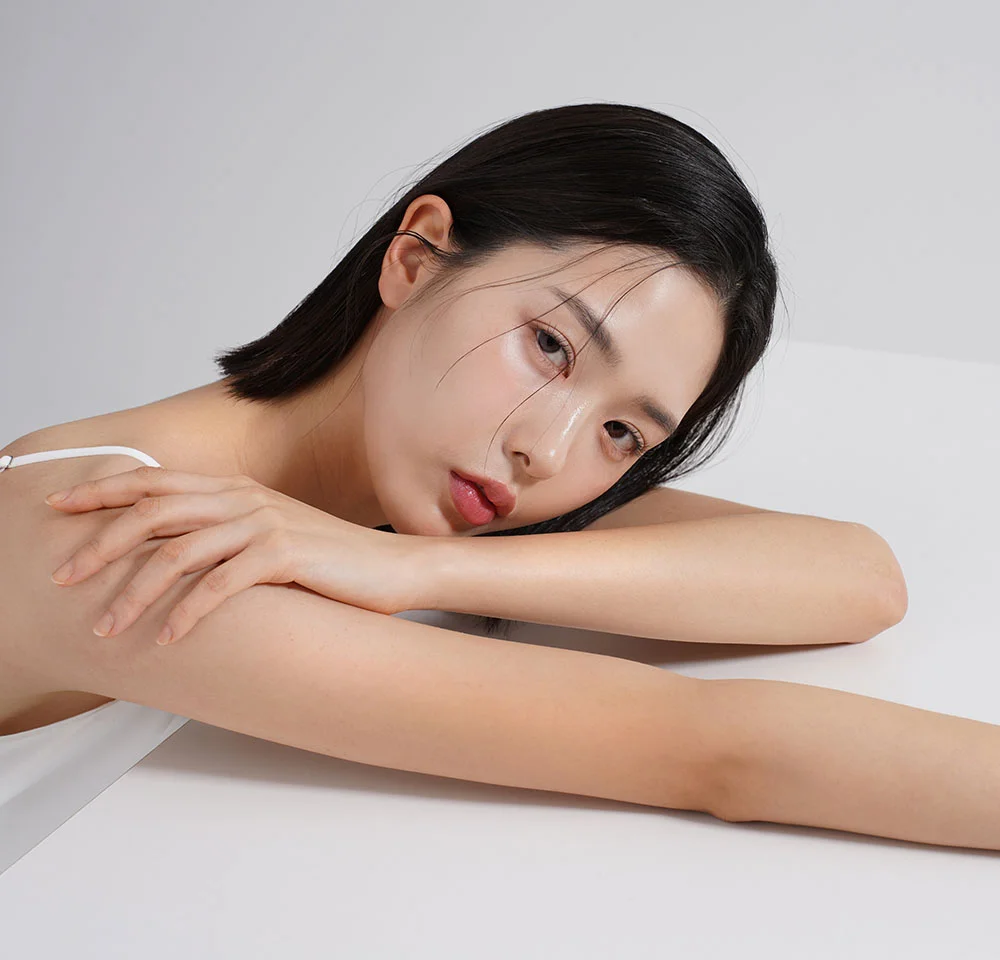 Portrait of a woman with straight, dark hair, resting her arms on a white surface and looking softly at the camera.