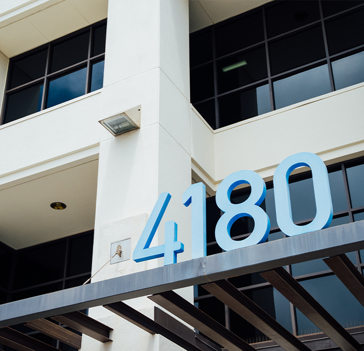 Low-angle shot of the entrance to a modern office building, with large, bright blue numbers "4180" mounted above the entryway.