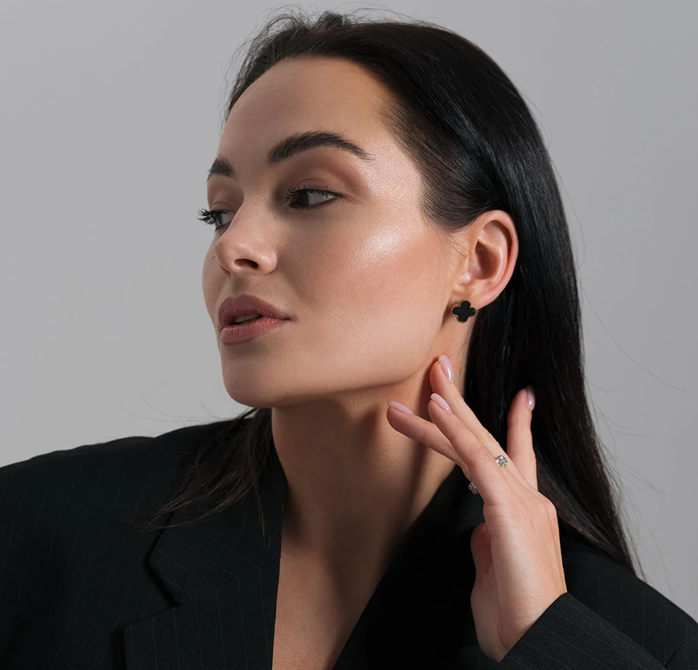 Profile portrait of a woman with long dark hair, wearing a black blazer and gently touching her jawline with her hand.