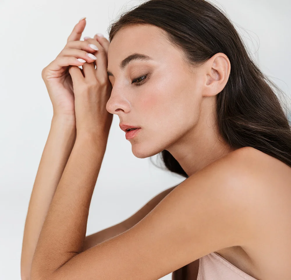 Profile shot of a woman with long dark hair and a soft pink top, resting her head on her hands with eyes closed.