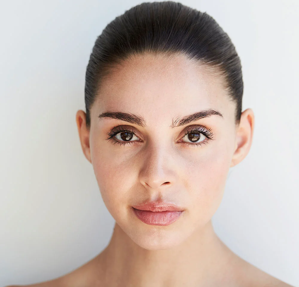 Headshot of a woman with dark hair pulled back, looking directly at the camera with a neutral expression against a white background.